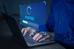 Mann mit blauem Hemd tippt etwas in Laptop vor ihm