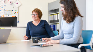 Zwei OCG Mitarbeiterinnen sitzen lächlend am Tisch in Meetingraum